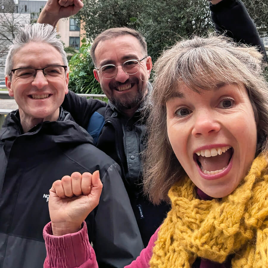 A group of three people outdoors, smiling and cheering, having solved a cryptic clue on their treasure hunt.