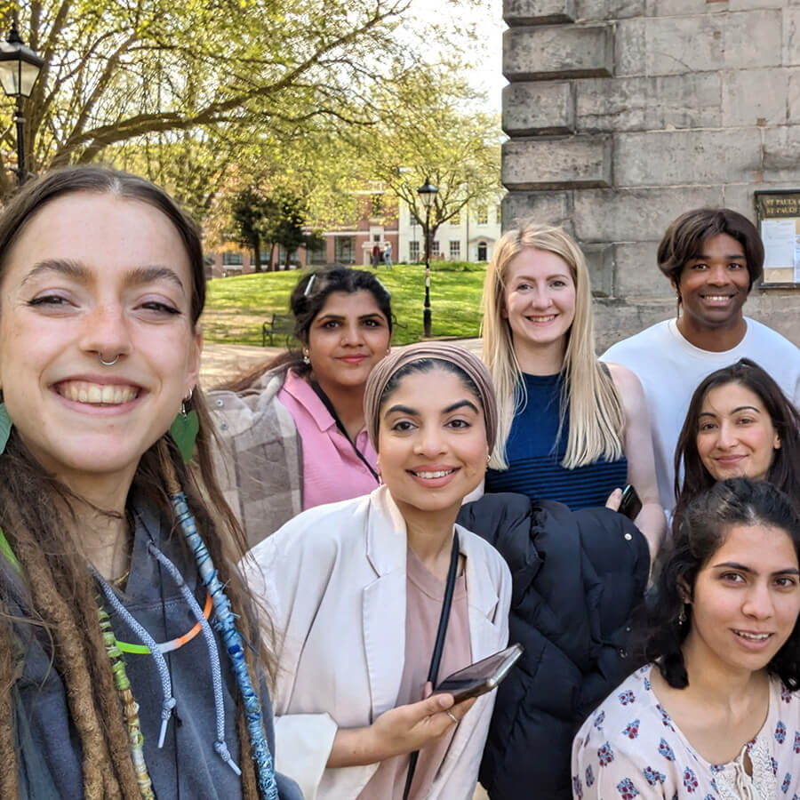 A diverse group of seven young people posing for a selfie in front of a historic building and a green park.