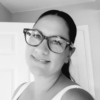 A black and white portrait of a woman wearing glasses, smiling at the camera